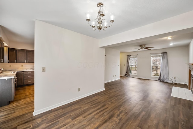 unfurnished living room with sink, ceiling fan with notable chandelier, and dark wood-type flooring