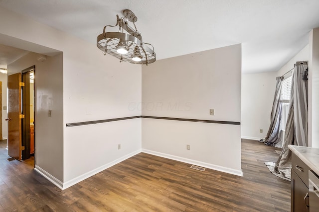 unfurnished dining area featuring dark hardwood / wood-style flooring and an inviting chandelier