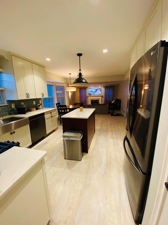 kitchen with tasteful backsplash, decorative light fixtures, black appliances, a kitchen island, and white cabinets