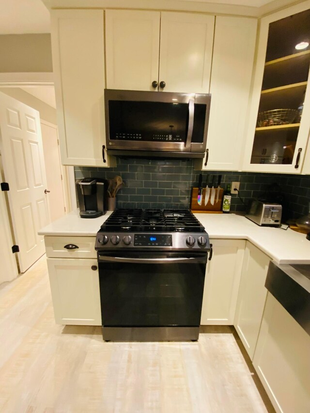 kitchen with backsplash, light hardwood / wood-style floors, white cabinets, and appliances with stainless steel finishes