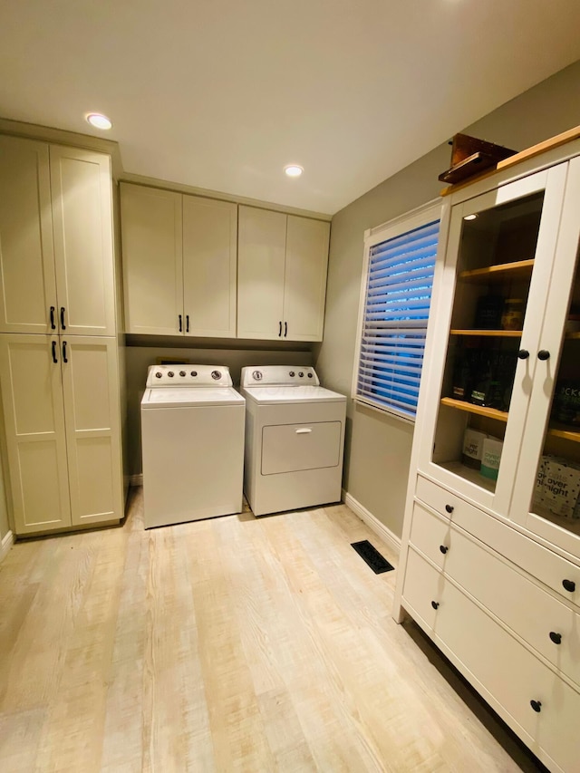 laundry area with cabinets, washing machine and dryer, and light wood-type flooring