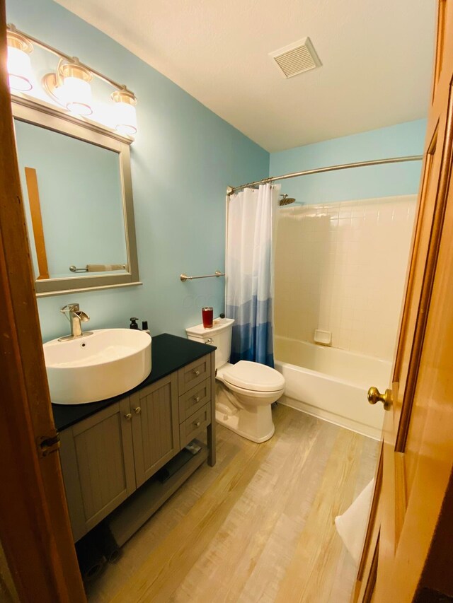 full bathroom featuring hardwood / wood-style flooring, shower / bath combo, vanity, and toilet