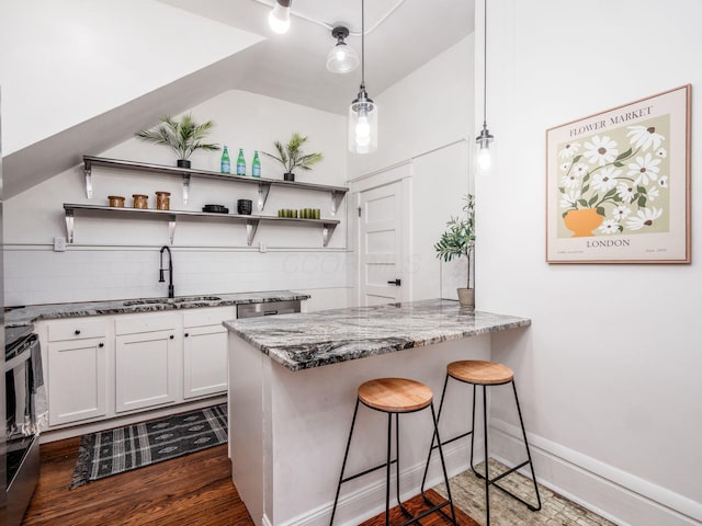 kitchen featuring decorative light fixtures, a breakfast bar area, white cabinets, dark stone counters, and kitchen peninsula