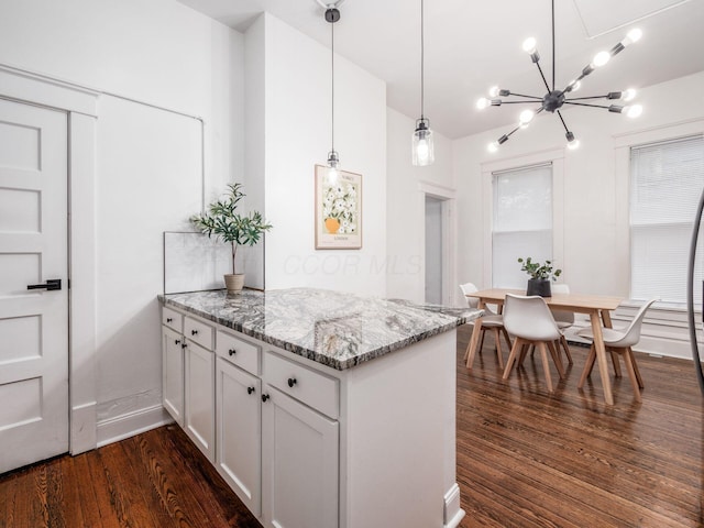 kitchen with white cabinets, dark hardwood / wood-style flooring, hanging light fixtures, light stone counters, and kitchen peninsula