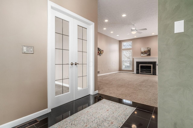 interior space featuring french doors, ceiling fan, a fireplace, and dark carpet