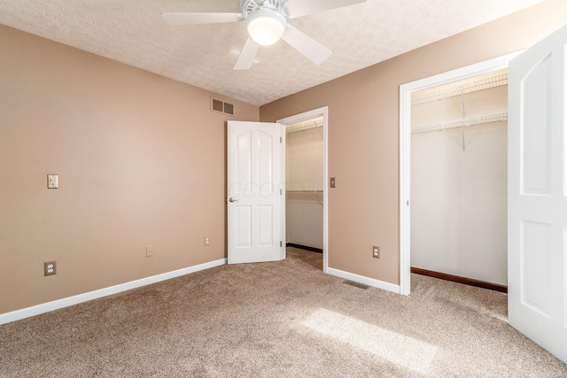 unfurnished bedroom featuring ceiling fan, a textured ceiling, multiple closets, and carpet flooring