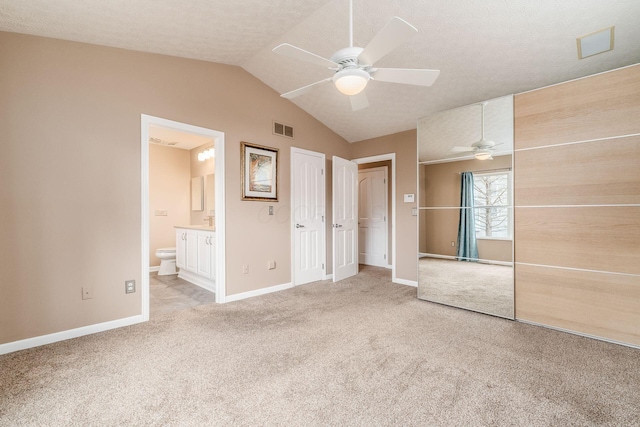 unfurnished bedroom featuring ensuite bath, light colored carpet, vaulted ceiling, a textured ceiling, and ceiling fan