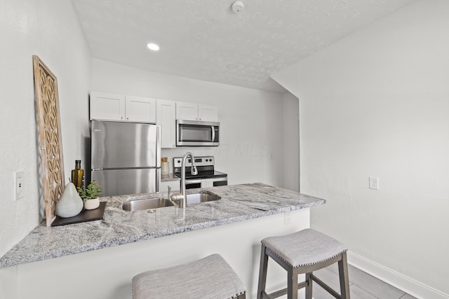 kitchen featuring appliances with stainless steel finishes, white cabinetry, a breakfast bar area, kitchen peninsula, and light stone countertops