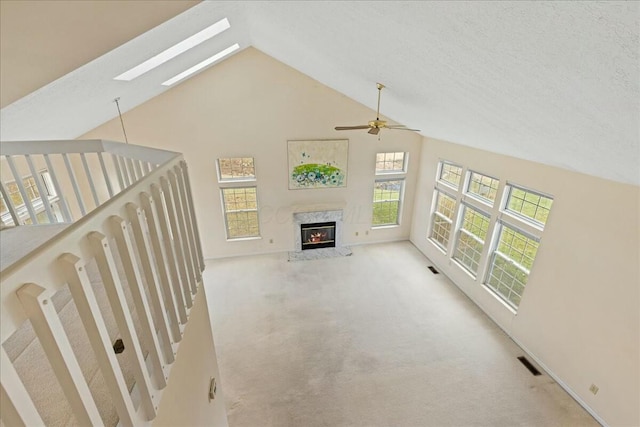 unfurnished living room featuring a fireplace, high vaulted ceiling, a skylight, ceiling fan, and light carpet