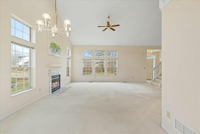 unfurnished living room featuring ceiling fan with notable chandelier, a high end fireplace, light colored carpet, and high vaulted ceiling