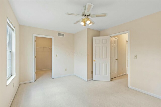 unfurnished bedroom with a walk in closet, light colored carpet, a closet, and ceiling fan