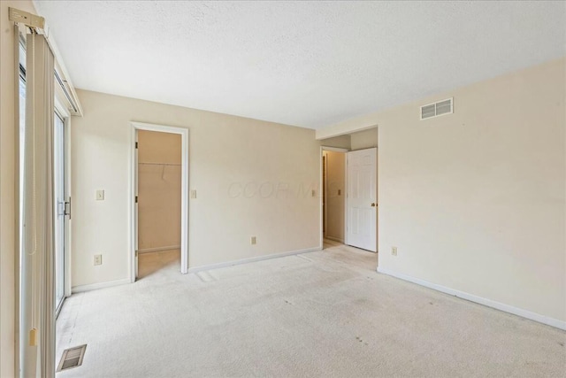 unfurnished bedroom featuring a walk in closet, light colored carpet, a textured ceiling, and a closet