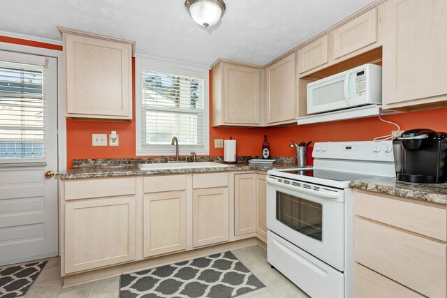 kitchen with light brown cabinetry, sink, light tile patterned floors, white appliances, and dark stone counters