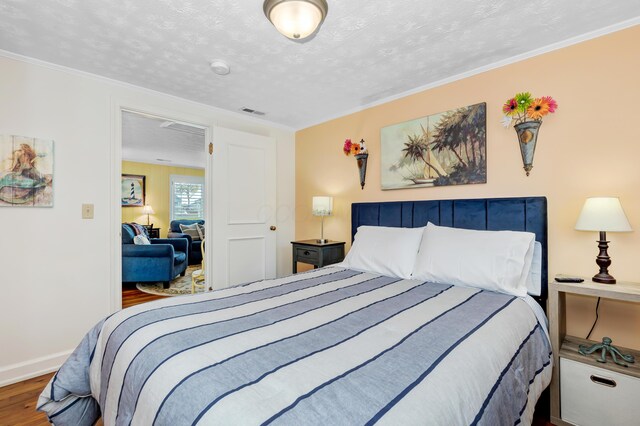 bedroom featuring crown molding, wood-type flooring, and a textured ceiling