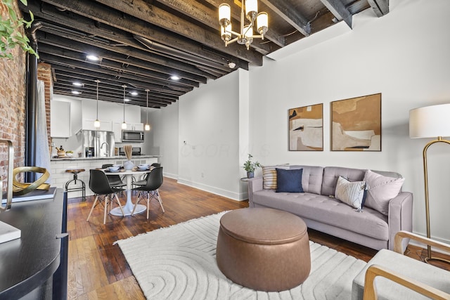 living room featuring dark hardwood / wood-style flooring, beamed ceiling, and an inviting chandelier