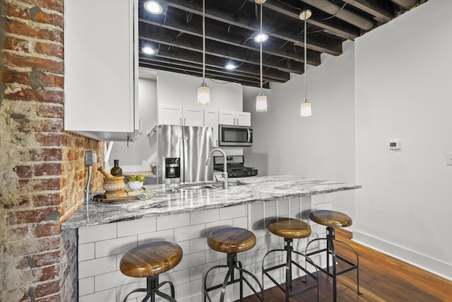 kitchen featuring a kitchen breakfast bar, kitchen peninsula, stainless steel appliances, light stone countertops, and white cabinets