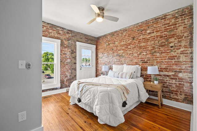 bedroom featuring hardwood / wood-style floors, ceiling fan, and brick wall