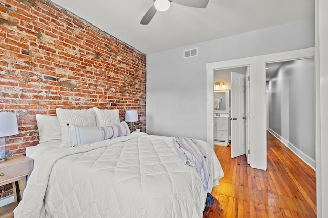 bedroom with hardwood / wood-style flooring, ensuite bathroom, ceiling fan, and brick wall