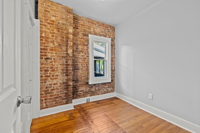 empty room featuring hardwood / wood-style flooring and brick wall