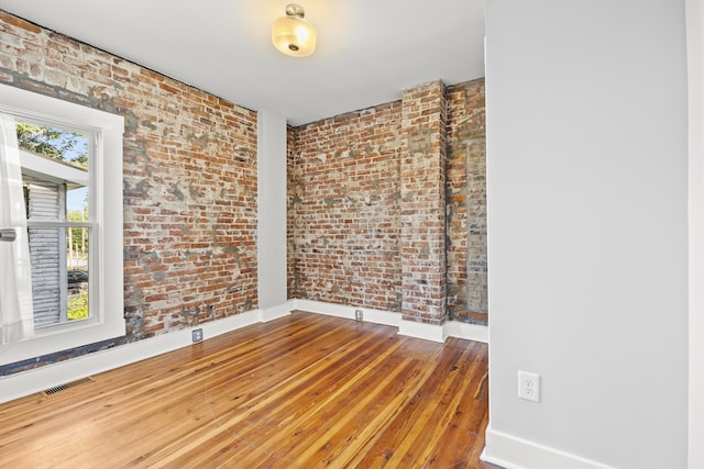 spare room featuring hardwood / wood-style flooring and brick wall