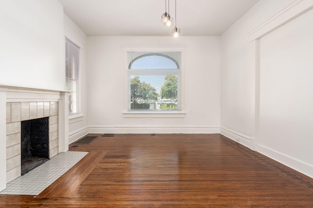 unfurnished dining area with dark wood-type flooring, a tiled fireplace, and a wealth of natural light