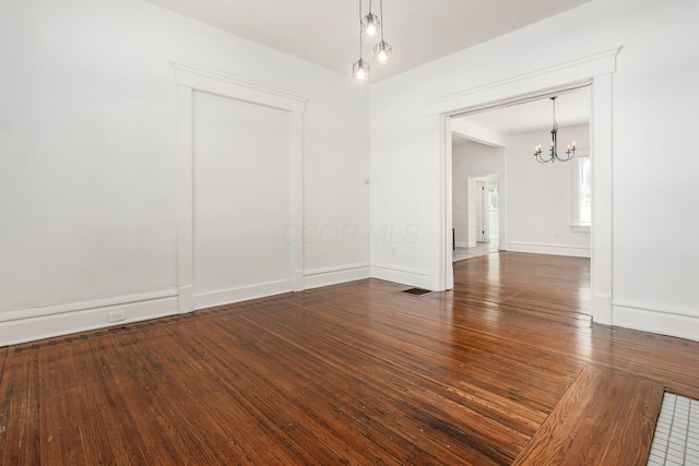 empty room featuring an inviting chandelier and dark hardwood / wood-style floors