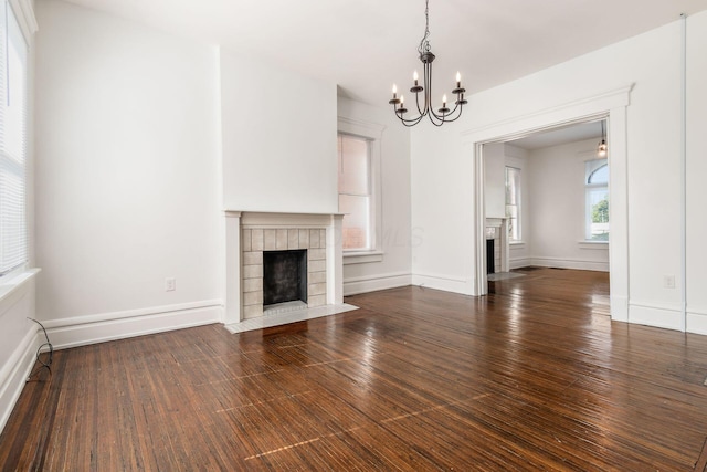 unfurnished living room with dark wood-type flooring, a fireplace, and a chandelier