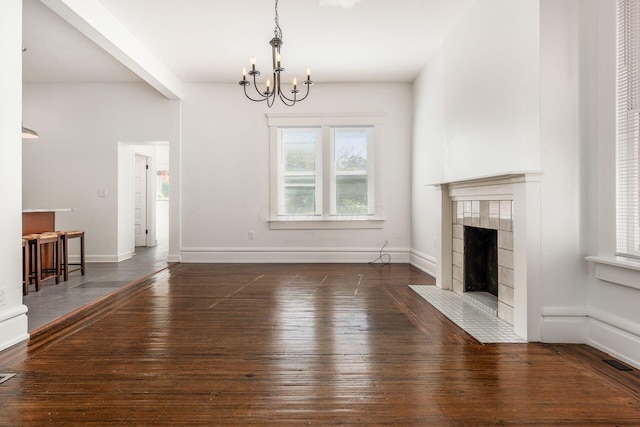 unfurnished living room featuring an inviting chandelier, dark hardwood / wood-style flooring, and a tiled fireplace