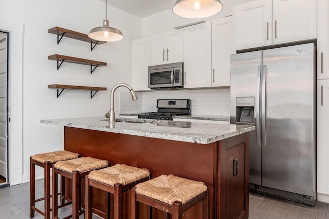 kitchen featuring white cabinetry, light stone counters, a breakfast bar, and appliances with stainless steel finishes