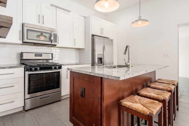 kitchen with a kitchen bar, white cabinetry, appliances with stainless steel finishes, light stone countertops, and a kitchen island with sink