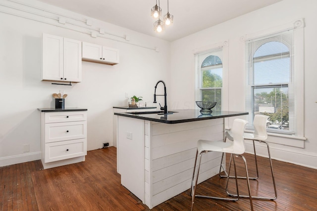 kitchen featuring a breakfast bar, decorative light fixtures, sink, white cabinets, and dark wood-type flooring