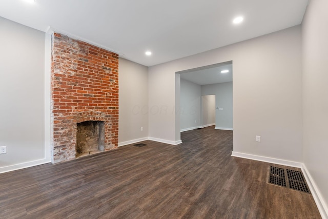 unfurnished living room featuring a brick fireplace and dark hardwood / wood-style floors