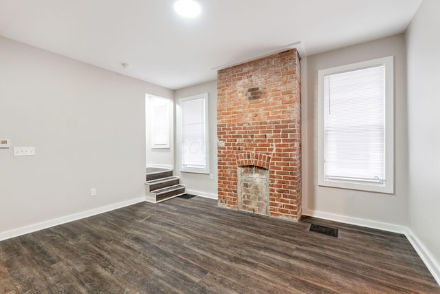 unfurnished living room with a fireplace, dark hardwood / wood-style floors, and a healthy amount of sunlight