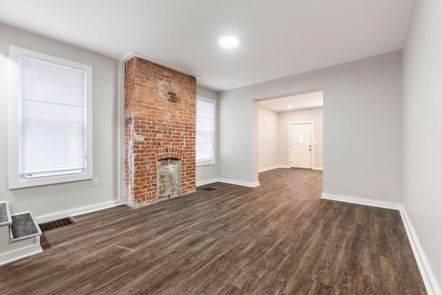 unfurnished living room featuring a brick fireplace and dark wood-type flooring