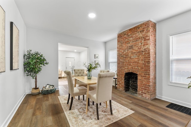 dining space featuring dark hardwood / wood-style floors and a brick fireplace