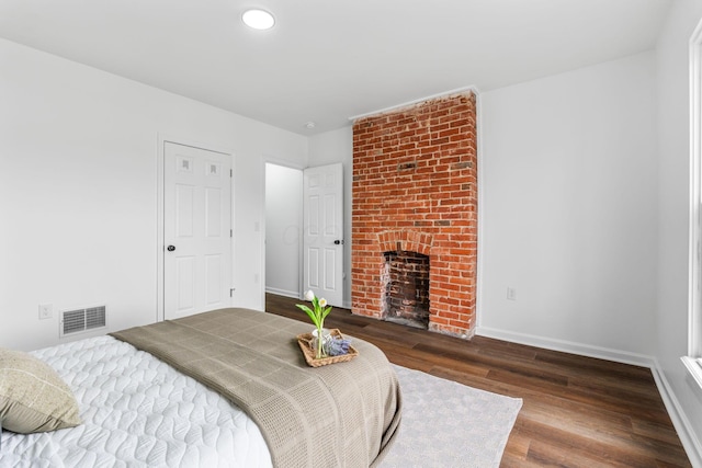 bedroom with dark hardwood / wood-style flooring and a brick fireplace