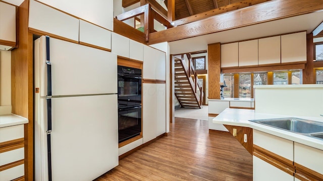 kitchen with double oven, white cabinets, a high ceiling, white fridge, and light hardwood / wood-style floors