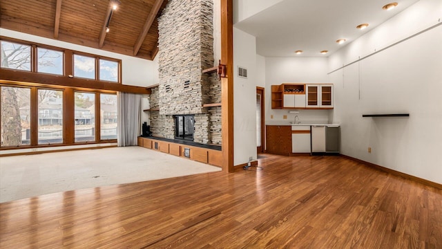 unfurnished living room featuring hardwood / wood-style flooring, high vaulted ceiling, a stone fireplace, wooden ceiling, and beamed ceiling