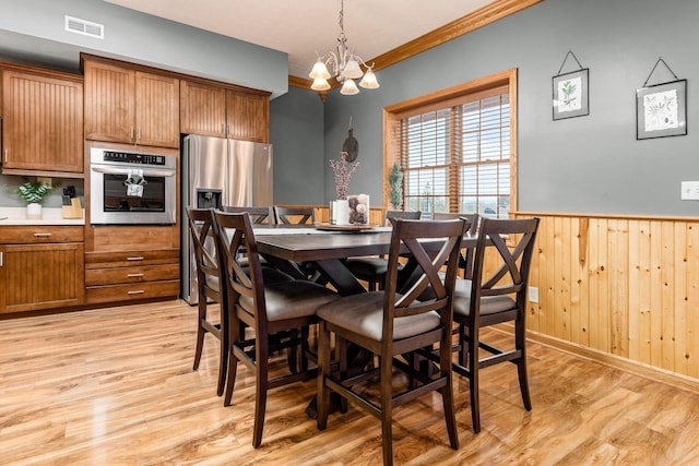 dining area with crown molding, a chandelier, light wood-type flooring, and wood walls