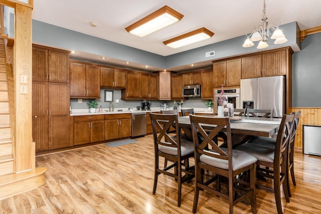 kitchen featuring an inviting chandelier, stainless steel appliances, a center island, decorative light fixtures, and light wood-type flooring