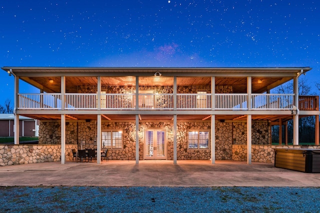 back house at night with a wooden deck, a patio area, and french doors