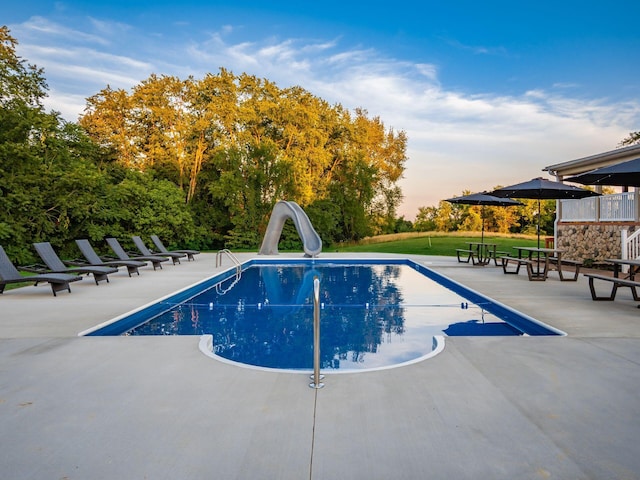 pool at dusk featuring a patio and a water slide