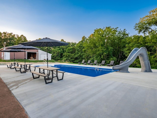 view of pool featuring a patio, a water slide, and a storage shed