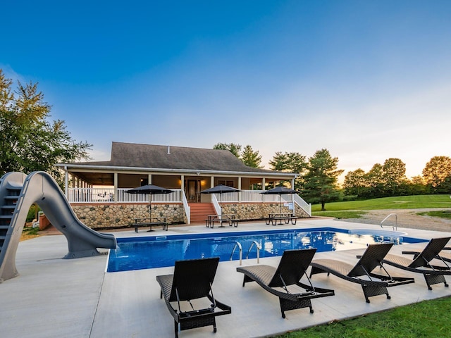 pool at dusk with a water slide and a patio area