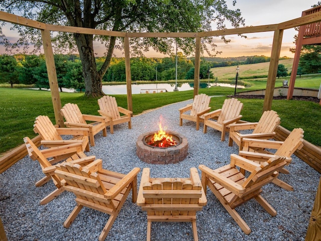 patio terrace at dusk with a water view, a yard, and a fire pit