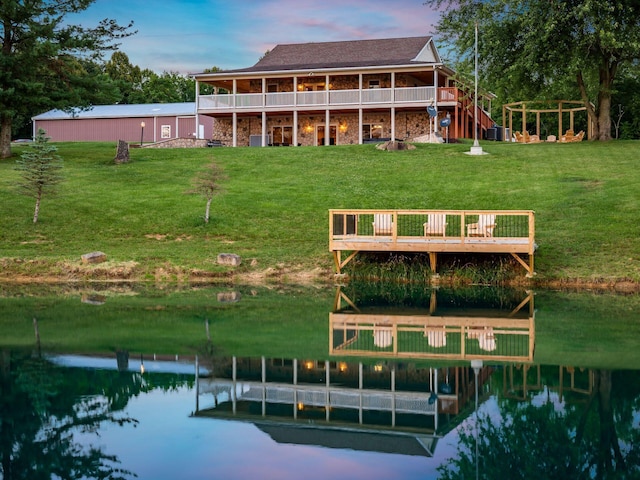 back house at dusk featuring a water view and a lawn