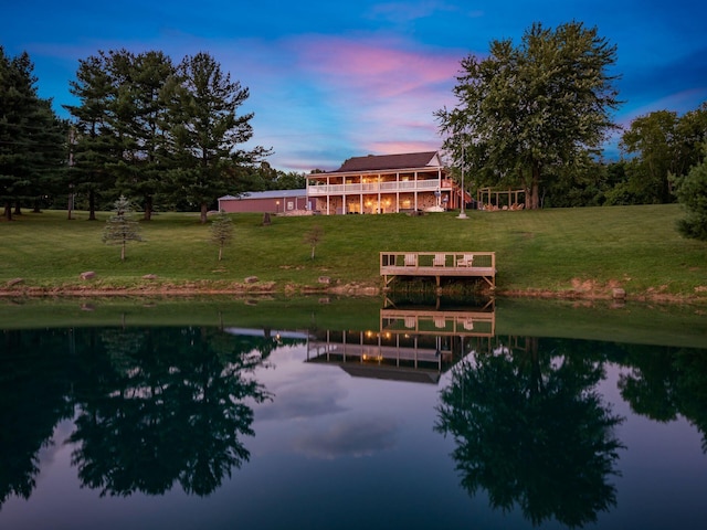 back house at dusk featuring a lawn and a water view