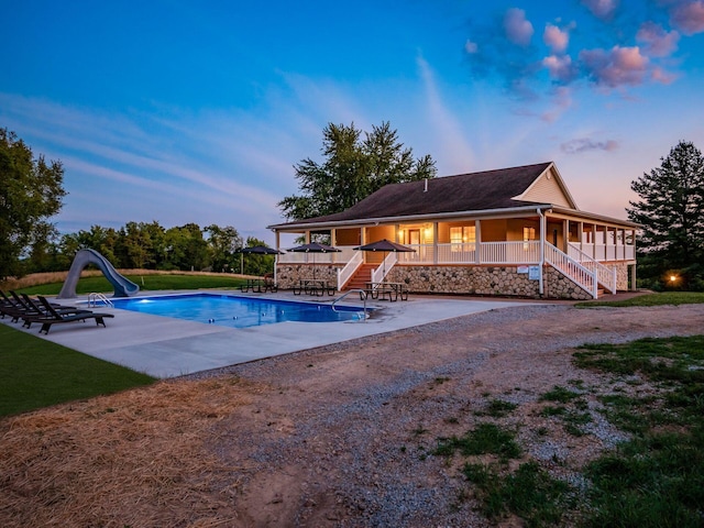 pool at dusk featuring a patio and a water slide