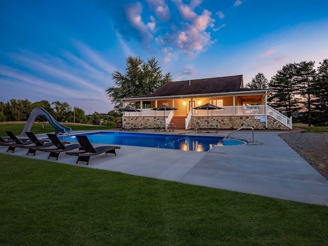 pool at dusk featuring a yard, a water slide, and a patio