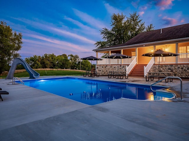 pool at dusk with a patio and a water slide